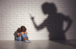 ängstliches Kind sitzt vor einer Wand, Mutter als bedrohlicher Schatten