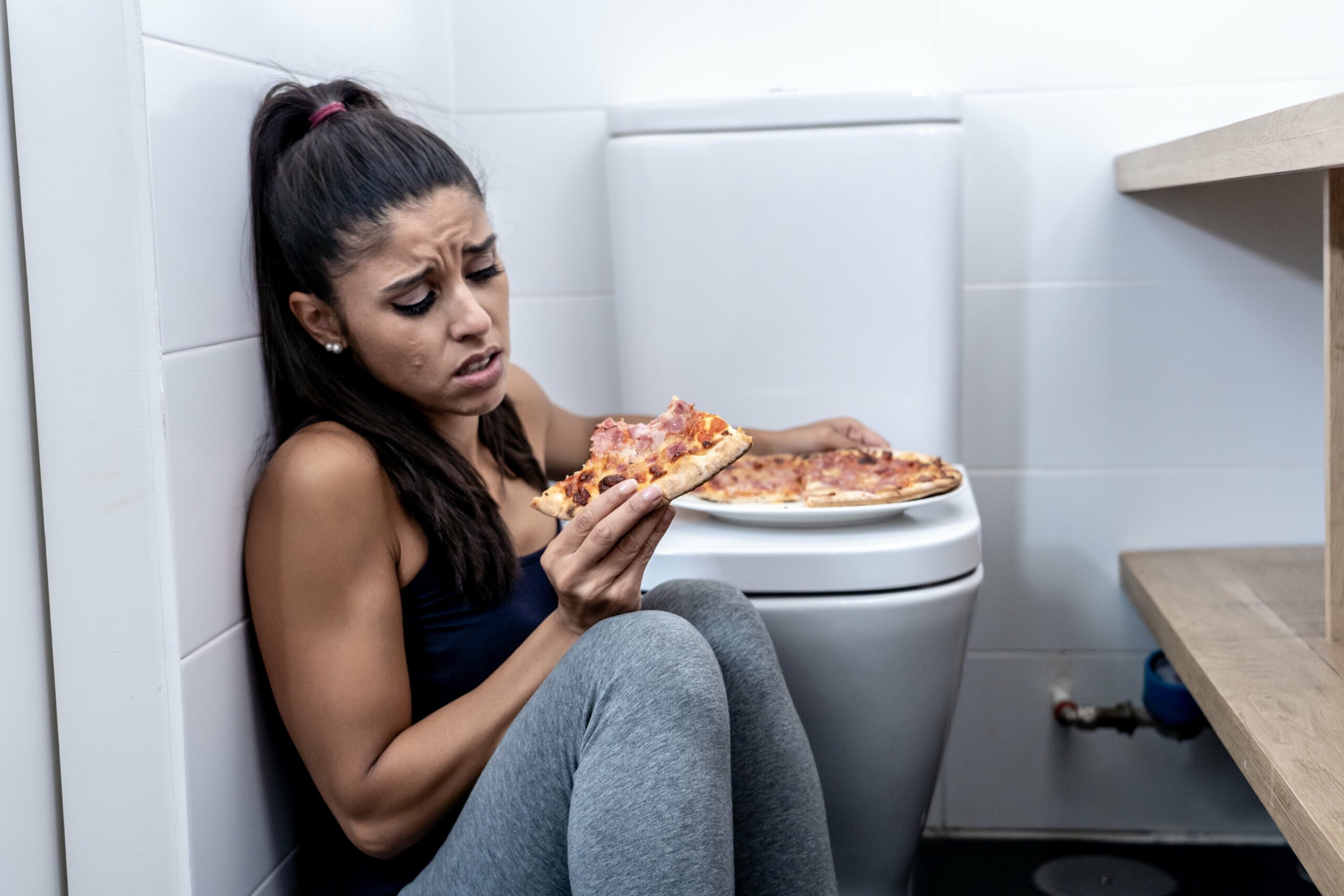 Bulimie-Mädchen mit Pizza leidend an Toilette
