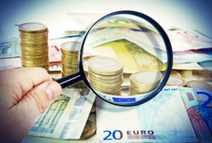 Lupe vor Euro-Münzen und Euro-Scheinen
