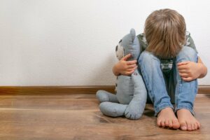 Junge sitzt traurig und verzweifelt mit seinem Teddy am Boden