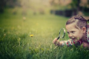 kleines Mädchen liegt mit einer Lupe im Gras