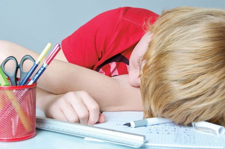 Kind liegt niedergeschlafen den Kopf neben die Schulaufgaben