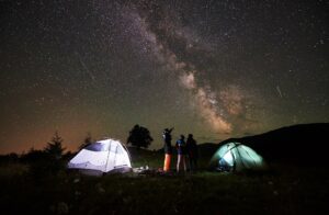 eine familie steht nachts neben zwei leuchtenden zelten und betrachtet den sternenhimmel