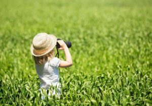 kleines Mädchen steht mit einem Fernglas im Gras