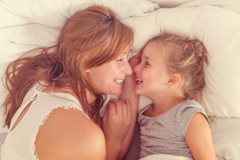 Mutter und Kind kuscheln im Bett und lachen