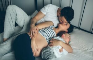 Schwangere Frau küsst ihren Mann, während der Sohn schläft